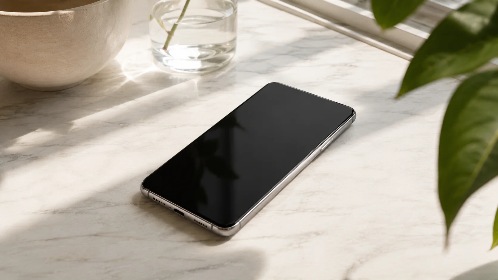 Smartphone modern pe blat de marmură albă cu lumină naturală și plantă în fundal