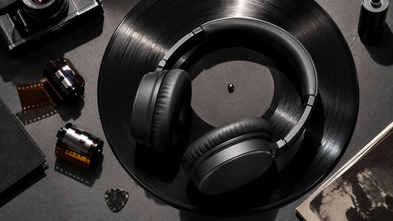 Căști wireless over-ear pe disc de vinil alături de role de film și pană de chitară